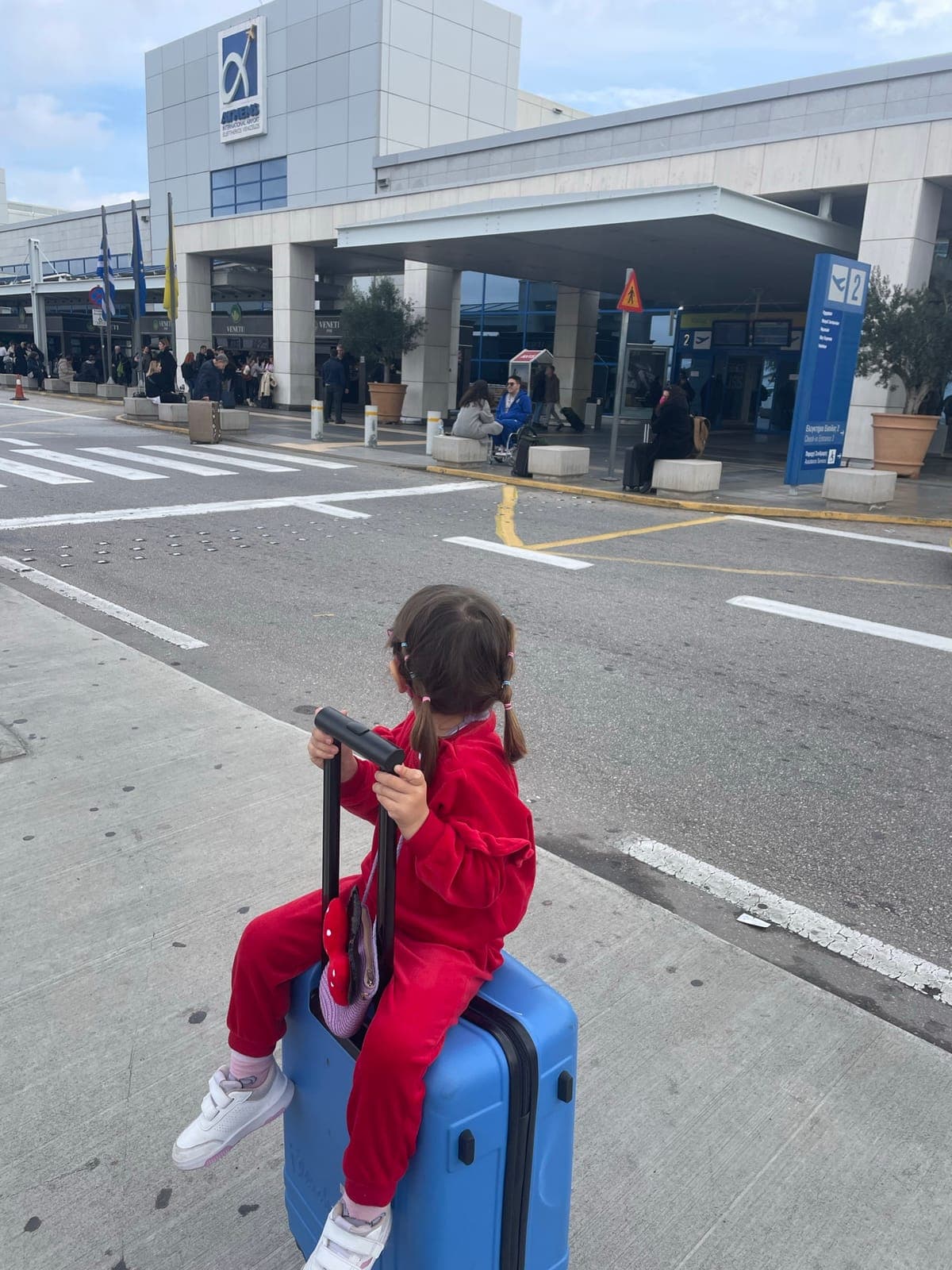 Katarina's daughter sitting on a suitcase outside the airport